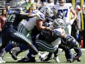 Dallas Cowboys running back Ezekiel Elliott, center, is tackled by Seattle Seahawks defensive end Dion Jordan, right, and linebacker Bobby Wagner, third from left, during the first half of an NFL football game, Sunday, Sept. 23, 2018, in Seattle.