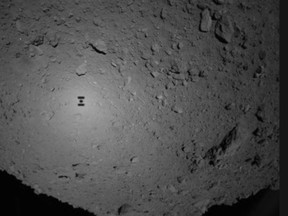 This image provided by the Japan Aerospace Exploration Agency (JAXA), shows the shadow, center left, of Japanese unmanned spacecraft Hayabusa2 over the asteroid Ryugu Friday, Sept. 21, 2018. The Japanese spacecraft Hayabusa2 released two small Minerva-II-1 rovers on the asteroid on Friday in a research effort that may provide clues to the origin of the solar system. JAXA said confirmation of the rovers' touchdown has to wait until it receives data from them on Saturday. (JAXA via AP)