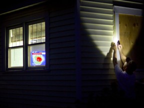 Rob Muller boards up his home as a satellite image of Hurricane Florence is broadcast on a television inside in Morehead City, N.C., Tuesday, Sept. 11, 2018.