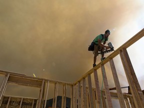 In this Thursday, Sept. 13, 2018 photo, Michael Evans works on framing the basement of a house as smoke from a wildfire rises to the south of the house in Elk Ridge, Utah.