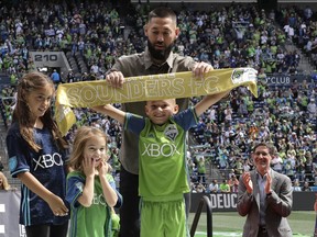 Seattle Sounders forward Clint Dempsey, top, helps his son Jackson hold up the golden scarf as his daughters Elyse, left, and Sophia, second from left, look on and Sounders owner Adrian Hanauer applauds at right, Saturday, Sept. 1, 2018, in Seattle, during a pre-match ceremony to honor Dempsey, who announced his retirement from professional soccer earlier in the week.