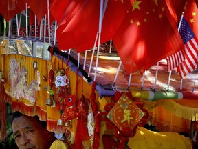 In this Sunday, Sept. 16, 2018, photo, a driver looks out from his trishaw decorated with an American flag and Chinese flags in Beijing. Chinese news reports have quoted a former finance minister as saying Beijing can disrupt American companies' operations by imposing "export controls" if it needs more leverage in its mounting tariff dispute with Washington.