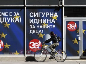 A woman rides a bicycle next to a poster "For European Macedonia", on a street in Skopje, Macedonia, Thursday, Sept. 27, 2018. Macedonians will vote Sunday in a referendum on whether to change the country's name to "North Macedonia", a move which would allow the Balkan country to qualify for NATO membership and also pave its way toward the European Union. The banner also reads in Macedonian "It is time for decision" and "A secure future for our children".