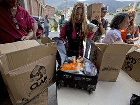 In this July 6, 2018 photo, employees of a government-supported cultural center receive boxes with subsided food distributed under a government program named "CLAP" in downtown Caracas, Venezuela. Some workers transfer the contents, cooking oil, flour, rice, canned tuna, to suitcases or backpacks for fear of becoming walking targets.