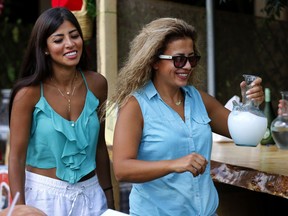 In this Saturday Sept. 8, 2018 photo, a woman carries arak in a traditional glass pitcher during a festival that celebrates Lebanon's national alcoholic drink, in the town of Taanayel, east Lebanon. At the festival several commercial companies and smaller boutique houses showcased their araks in a celebration aimed at promoting the drink to the young.