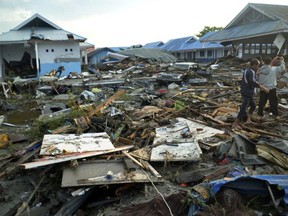 Indonesian men survey the damage following earthquakes and a tsunami in Palu, Central Sulawesi, Indonesia, Saturday, Sept. 29, 2018. A tsunami swept away buildings and killed large number of people on the Indonesian island of Sulawesi, dumping victims caught in its relentless path across a devastated landscape that rescuers were struggling to reach Saturday, hindered by damaged roads and broken communications.