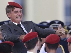 FILE - In this April 19, 2018 file photo, presidential hopeful, conservative Brazilian lawmaker Jair Bolsonaro flashes two thumbs up as he poses for a photo with cadets during a ceremony marking Army Day, in Brasilia, Brazil.  Bolsonaro, the leading candidate in Brazil's presidential race was discharged from the hospital Saturday, Sept. 29, 2018, where he was being treated for a knife wound to his abdomen.