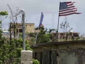 FILE - In this May 16, 2018 file photo, deteriorated U.S. and Puerto Rico flags fly on a roof eight months after the passing of Hurricane Maria in the Barrio Jacana Piedra Blanca area of Yabucoa, a town where power was knocked out by the storm. Though President Donald Trump continued one year after the storm to assert that his administration's efforts in Puerto Rico were "incredibly successful," both the local and federal governments have been heavily criticized for inadequate planning and post-storm response.