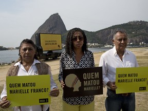 The parents of slain councilwoman Marielle Franco, Marinete da Silva, left, Antonio Francisco da Silva, right, and Jurema Werneck, director of Amnesty International Brazil, pose for a photo holding signs with a message that reads in Portuguese: "Who killed Marielle Franco?" during a demonstration marking the 6th month since she was killed, in Rio de Janeiro, Brazil, Friday, Sept. 14, 2018. Elected in 2016, the 38-year-old Franco was a member of the left-leaning Socialism and Liberty Party and known for social work in poor and marginalized shantytowns, or favelas, and for her outspokenness against police violence.