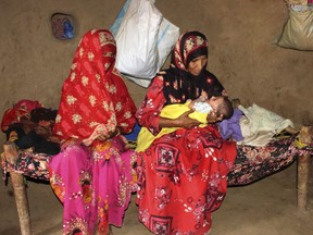 In this Sept. 22, 2018 photo, Amna Ali, right, mother of 3-year-old Zaifa Shouib, who was the fifth child known to have died in the district this year of malnutrition-related illness, sits in her hut holding a baby in Khayran al-Maharq, Hajjah, Yemen. At a local medical facility which did not have enough supplies, Zaifa's father was told she had to be taken to a hospital further away to treat kidney complications. He had no way to pay for transportation there.