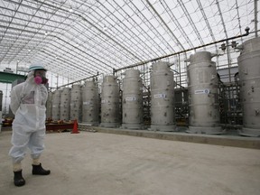 In this Nov. 12, 2014 file photo, a Tokyo Electric Power Co. (TEPCO) official wearing a radioactive protective gear stands in front of Advanced Liquid Processing Systems during a press tour at the Fukushima Dai-ichi nuclear power plant in Okuma, Fukushima Prefecture, northeastern Japan.