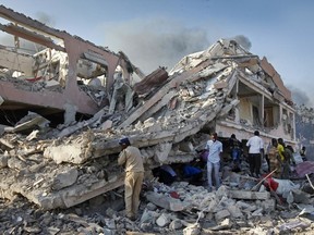 FILE - In this Saturday, Oct 14, 2017, file photo, people gather to search for survivors by destroyed buildings at the scene of a blast in the capital Mogadishu, Somalia. Somalia is marking the first anniversary of one of the world's deadliest attacks since 9/11, a truck bombing in the heart of Mogadishu that killed well over 500 people. The Oct. 14, 2017 attack was so devastating that the al-Shabab extremist group that often targets the capital never claimed responsibility amid the local outrage. As Somalis gather at a new memorial with a minute of silence, local media report that the man accused of orchestrating the bombing has been executed.