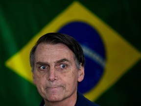 Brazil's right-wing presidential candidate for the Social Liberal Party (PSL) Jair Bolsonaro gestures in front of the Brazilian flag as he prepares to cast his vote during the general elections, in Rio de Janeiro, Brazil, on October 7, 2018.