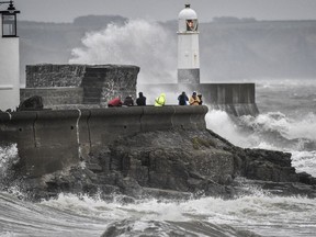 People watch as waves crash against the harbour wall, in Porthcawl, South Wales, Saturday, Oct. 13, 2018.