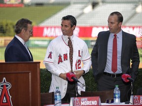 Joined by Los Angeles Angels owner Arte Moreno, left, and general manager Billy Eppler, right, join the team's new manager Brad Ausmus as he puts on a jersey during a news conference Monday, Oct. 22, 2018, in Anaheim, Calif. The former Tigers skipper replaces Mike Scioscia with plans to boost a big-budget team with no playoff victories since 2009.