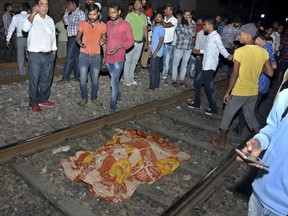 The body of a victim of a train accident lies covered in cloth on a railway track in Amritsar, India, Friday, Oct. 19, 2018.