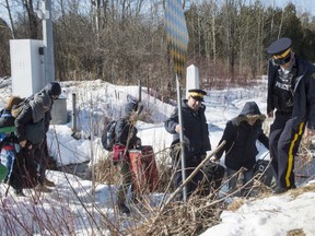 RCMP officers help a family of asylum claimants as they cross the border into Canada from the United States, Monday, February 20, 2017 near Hemmingford, Que. Canadian Immigration officials were made fully aware of heavy-handed plans to crack down on "illegal aliens" by Trump administration, but despite this, an internal review of the Safe Third Country agreement determined the United States remains a safe country for asylum seekers.