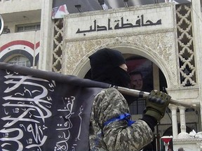 FILE - In this file photo posted on the Twitter page of Syria's al-Qaida-linked Nusra Front on March 28, 2015, a fighter from Syria's al-Qaida-linked Nusra Front holds his group flag as he stands in front of the governor building in Idlib province, north Syria. Turkey and Russia appear to have succeeded in creating a demilitarized zone along the frontlines of Syria's flashpoint Idlib region, after rebels and an al-Qaida-linked alliance pulled back their heavy weaponry in accordance with the agreement. (Al-Nusra Front Twitter page via AP, File)