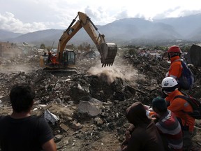 FILE - In this Thursday, Oct. 11, 2018, file photo, rescue workers watch as a heavy machine dig through rubble searching for earthquake victims at Balaroa neighborhood in Palu, Central Sulawesi, Indonesia, Thursday, Oct. 11, 2018. Indonesia's disaster agency says helicopters are dropping disinfectant on neighborhoods in the earthquake and tsunami-stricken city of Palu to reduce disease risks from the thousands of victims believed buried in obliterated communities.