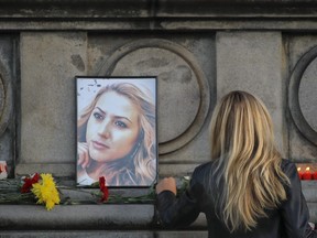 A woman places flowers next to a portrait of slain television reporter Viktoria Marinova during a vigil at the Liberty Monument in Ruse, Bulgaria, Monday, Oct. 8, 2018.