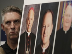 Tom Emens listens to speakers as he stands next to photos of San Francisco Archbisop Salvatore Cordileone, from left, Oakland Bishop Michael Barber and San Jose Bishop Patrick McGrath at a news conference in San Francisco, Tuesday, Oct. 23, 2018. A law firm suing California bishops for the records of priests accused of sexual abuse has compiled a report of clergy in the San Francisco Bay Area it says are accused of misconduct.