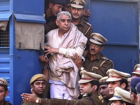 FILE - In this Nov. 20, 2014 file photo, controversial religious leader Sant Rampal stands by the door of a police van as he is brought to a court, surrounded by police personnel in Chandigarh, India. A court in northern India on Tuesday, oct. 16, 2018, has sentenced the Hindu guru and 14 followers to life imprisonment in the deaths of four women and a child at his sprawling ashram. Rampal was arrested in 2014 following a days-long standoff between law enforcers and his supporters in which six people died and hundreds were injured.