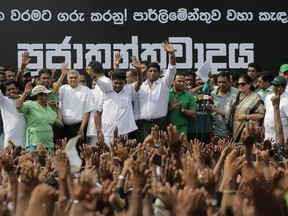 Sri Lanka's sacked prime minister Ranil Wickremesinghe, third from left in white shirt and black trousers, waves to his supporters along with law makers supporting him during a protest rally outside the prime ministers official residence in Colombo, Sri Lanka, Tuesday, Oct. 30, 2018. Thousands of supporters of wickremesinghe gathered in capital demanding president Maithripala Sirisena to convene the parliament immediately. Back drop in Sinhalese reads " Respect the mandate! Convene the parliament ! Democracy ".
