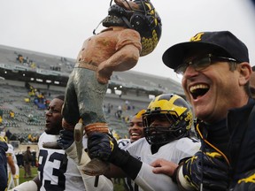 CORRECTS IDENITY OF PLAYER AT LEFT TO MICHIGAN DEFENSIVE LINEMAN LAWRENCE MARSHALL (93) INSTEAD OF MICHIGAN TIGHT END ZACH GENTRY (83) - Michigan defensive lineman Lawrence Marshall (93),  linebacker Devin Bush, and head coach Jim Harbaugh walk off the field with the Paul Bunyan trophy after an NCAA college football game against Michigan State, Saturday, Oct. 20, 2018, in East Lansing, Mich. Michigan won 21-7.