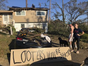 In this Oct. 10, 2018 photo Shauna Benefield and Alex Edwards stand near a sign warning looters in front of their house in Marianna, Fla., which was damaged by fallen trees during Hurricane Michael. Armed looters are targeting homes and businesses that remain without electricity after being ravaged by Hurricane Michael a week ago.