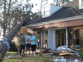 Rex Buzzett, far left, his son Josh Buzzett and neighbor Hilda Duren stand outside the Buzzett's home, Thursday, Oct. 11, 2018, that was gutted by a storm surge in Port St. Joe, Fla. Hurricane Michael devastated several homes overlooking the Gulf of Mexico in Port St. Joe, while largely sparing residents of the neighboring Gulf community of Apalachicola.