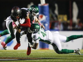 Saskatchewan Roughriders' Derrick Moncrief, right, and Cameron Judge, centre, bring down Calgary Stampeders' Markeith Ambles during CFL football action in Calgary, Saturday, Oct. 20, 2018.