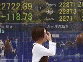 A woman walks by an electronic stock board of a securities firm in Tokyo, Thursday, Oct. 18, 2018. Shares fell Thursday in Asia after a retreat on Wall Street driven by a sell-off of technology shares, homebuilders and retailers. A report of weaker Japanese exports in September underscored uncertainties over the outlook for trade.