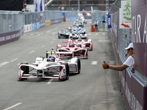 FILE - In this Sunday, July 15, 2018 file photo, a Formula E safety worker, right, gives a thumbs-up to drivers during the second of two auto races in the Formula E championship, in the Brooklyn borough of New York. Urging a rapid response to the latest global warming concerns, Nico Rosberg said Monday Oct. 15, 2018, he predicts a merger eventually between the fuel-guzzling Formula One championship and the electric motorsport series.