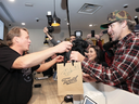 Canopy Growth CEO Bruce Linton, left, passes a bag with the first legal cannabis for recreation use sold in Canada to Nikki Rose and Ian Power at the Tweed shop in St. John's N.L. at 12:01 am NDT on Oct. 17, 2018.