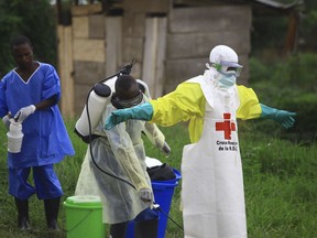 FILE - In this Sunday, Sept 9, 2018 file photo, a health worker sprays disinfectant on his colleague after working at an Ebola treatment centre in Beni, Eastern Congo. The World Health Organization is announcing on Wednesday, Oct. 17 whether Congo's latest outbreak of the deadly Ebola virus should be declared a global health emergency.