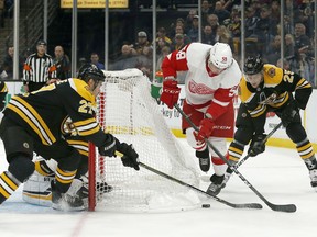 Detroit Red Wings left wing Tyler Bertuzzi (59) tries to move the puck around the net as Boston Bruins players John Moore (27) and Brandon Carlo (25) defend during the first period of an NHL hockey game, Saturday, Oct. 13, 2018, in Boston.