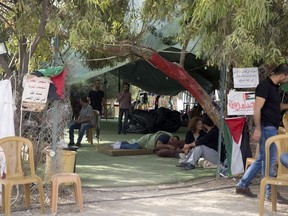 Palestinians activists sit in front of a tent for supporters of the West Bank Bedouin community of Khan al-Ahmar, Sunday, Oct. 21, 2018. Israeli Prime Minister Benjamin Netanyahu said Sunday he has decided to postpone the planned demolition of a West Bank hamlet to allow time for a negotiated solution with its residents, in a move that appeared aimed at staving off the fierce international condemnation such a demolition would likely entail.