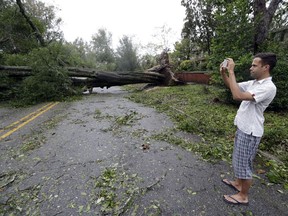 FILE - In a  Friday, Sept. 14, 2018 file photo, Shane Fernando takes a photo of fallen trees near his home in Wilmington, N.C., after Hurricane Florence made landfall.  Fernando is worried about the approach of Hurricane Michael because he sustained tree damage to his house in Florence and has tarps covering parts of the exterior.