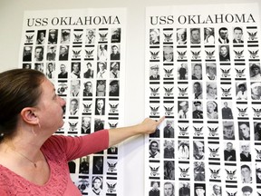 In this Sept. 18, 2018 photo, Dr. Carrie Brown, forensic anthropologist and director of the USS Oklahoma Project at the Defense POW/MIA Accounting Agency (DPAA) Identification laboratory, points to images on posters showing the names and photos of the victims of the USS Oklahoma, sunk by the Japanese in Pearl Harbor. Decades after they died, the military is seeing a surge in identifications of U.S. service members who had been classified as missing in action.