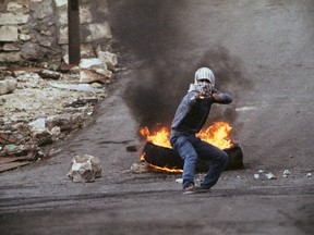 FILE - In this Jan. 14, 1988, file photo taken by Max Nash, a Palestinian teenager aims a slingshot in front of a blazing tire at photographers and Israeli soldiers in the Israel-occupied West Bank town of Nablus. Nash, who covered the conflicts in Southeast Asia and the Middle East and helped nurture a new generation of female photojournalists during more than 40 years with The Associated Press, died Friday, Sept. 28, 2018, after collapsing at home. He was 77.
