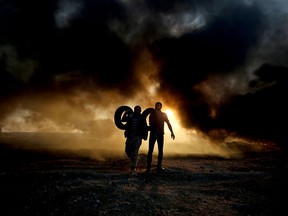 Palestinian protesters carry tires as smoke billows from burning tires at the Israel-Gaza border, east of Gaza City, on Oct.12, 2018.