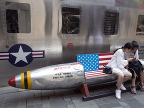 FILE - In this July 6, 2018, file photo, Chinese women look at phone near a rocket shaped bench with an American flag used as a marketing gimmick for a U.S. apparel shop in Beijing. The U.S. will not send a high-ranking official to attend a major investment fair in China next month, the U.S. Embassy said Wednesday, Oct. 24, 2018, in a move underscoring worsening trade frictions between the world's two largest economies.