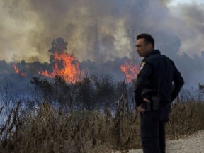 Israeli policeman watches a fire started by a balloon with attached burning cloth launched by Palestinians from Gaza Strip in Karmia nature reserve park near Israel and Gaza border, Thursday, Oct. 11, 2018.