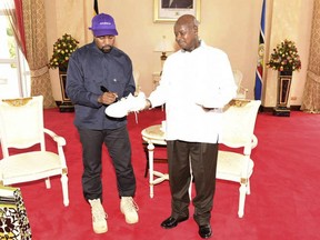 In this photo taken Monday, Oct. 15, 2018 Kanye West autographs a pair of his sneakers as a gift to Uganda's President Yoweri Museveni, right, at State House in Entebbe, Uganda. Museveni said he and West held "fruitful discussions" about promoting tourism and arts in the East African nation in which the rapper is said to be recording music in a tent.