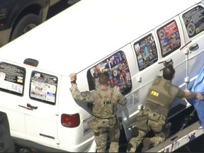 This frame grab from video provided by WPLG-TV shows FBI agents covering a van after the tarp fell off as it was transported from Plantation, Fla., on Friday, Oct. 26, 2018, that federal agents and police officers have been examining in connection with package bombs that were sent to high-profile critics of President Donald Trump. The van has several stickers on the windows, including American flags, decals with logos and text. (WPLG-TV via AP)