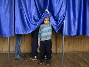 A child lifts the courtain of a voting booth as his father casts his vote, in Ciorogarla, Romania, Sunday, Oct. 7, 2018. Romanians are voting Sunday around the country for a second day on a constitutional amendment that would make it harder to legalize same-sex marriage.