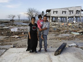 In this Oct. 5, 2018, photo, Musrifah, left, and her husband Hakim, right, and their daughter Syafa Ramadi pose where their house once stood before a massive earthquake and tsunami hit their seaside village in Palu, Central Sulawesi, Indonesia. The family lost their son. The 7.5 magnitude quake triggered not just a tsunami that leveled huge swathes of the region's coast, but a geological phenomenon known as liquefaction, making the soil move like liquid and swallowing entire neighborhoods.