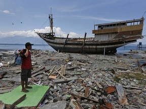 A man carries his belongings he scavenged from the ruins of his house as a boat swept ashore by tsunami rests on the beach in Wani village on the outskirt of Palu, Central Sulawesi, Indonesia, Wednesday, Oct. 10, 2018.