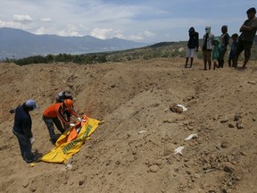 A rescue worker helps people who are looking for their missing relatives to identify a body at a mass grave for earthquake and tsunami victims in Palu, Central Sulawesi, Indonesia, Friday, Oct. 5, 2018. A 7.5 magnitude earthquake rocked the city on Sept. 28, triggering a tsunami and mud slides that killed a large number of people and displaced tens of thousands others.