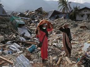 Indonesian women stand on the rubble as they look for what's left from a relative's house at Balaroa neighborhood in Palu, Central Sulawesi, Indonesia, Thursday, Oct. 11, 2018. Indonesia's search for victims buried in neighborhoods annihilated by an earthquake and tsunami is nearing its end almost two weeks after the double disasters hit the remote city.